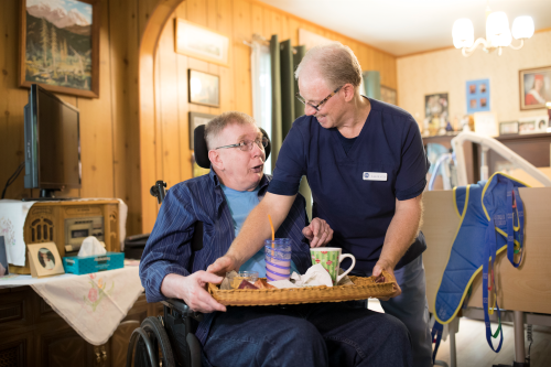 VON homecare worker smiling at a client in a wheelchair as they remove a dinner tray from the client's lap, set in a home environment. 