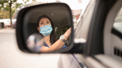 A masked individual at their wheels, photographed through their rear-view mirror