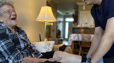 Continuing Care Assistant applying a compression stocking on a client on their sofa in their home.