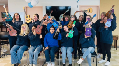 a large group of people holding up their ukuleles and smiling