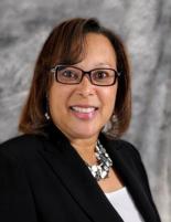 Headshot of Cynthia Dorrington wearing a white blouse, necklace and black blazer, grey marble textured background.