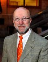 Headshot of Darrel Pink wearing a white dress shirt, orange tie and tweed blazer, courtroom background