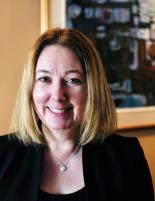 Image of Wendy Steele wearing a black blouse and black blazer with a painting in the background